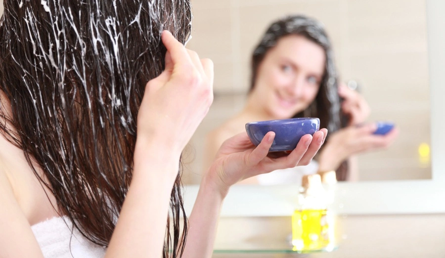 Mladá žena si aplikuje masku na vlasy